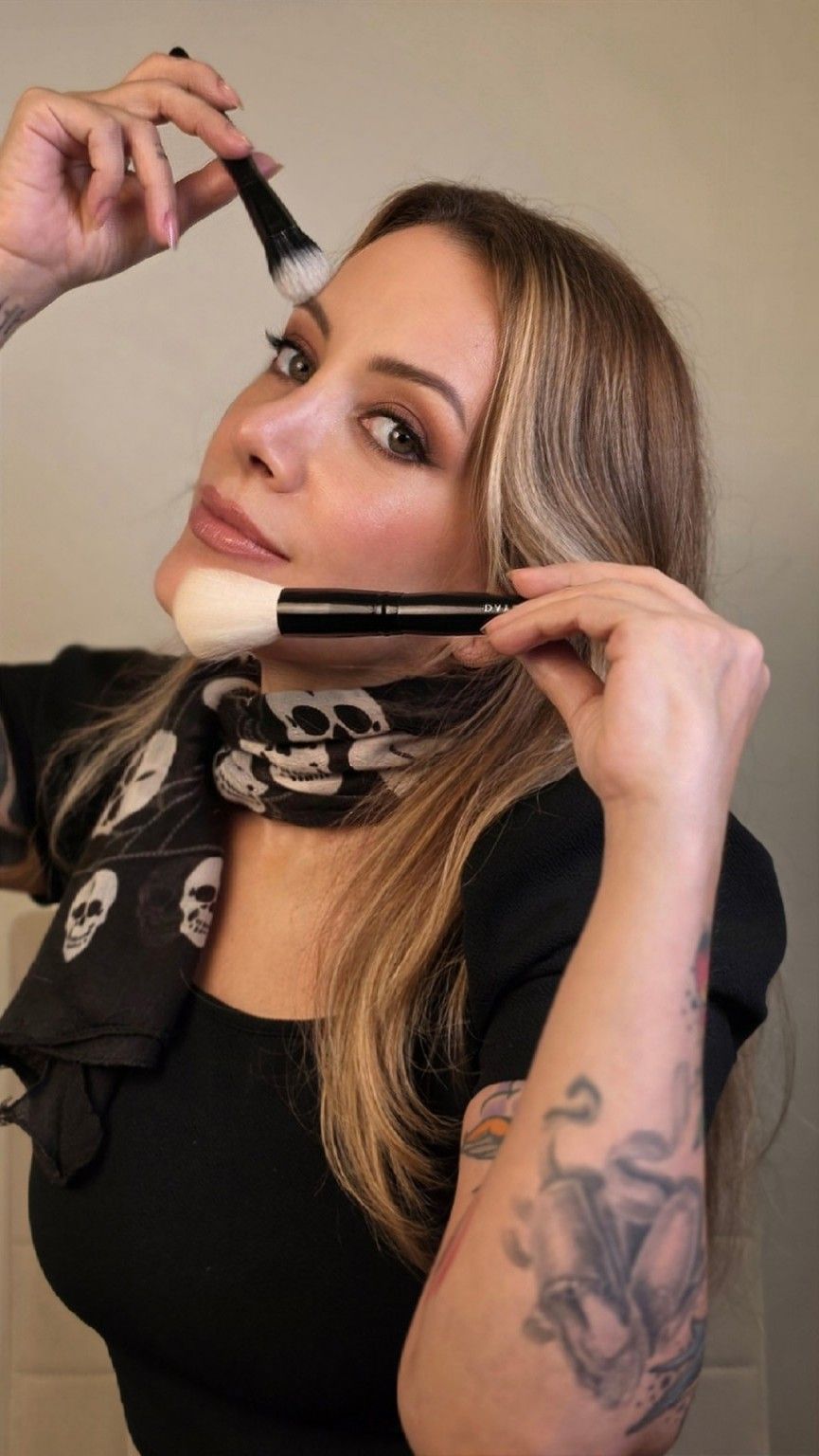 Stella Montero, maquiadora, segurando dois pincéis de maquiagem junto ao rosto